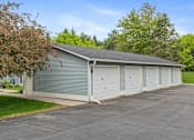Thumbnail 6 of 27 - A two-car garage with a grey roof and white doors is surrounded by a paved driveway and greenery.