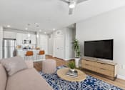 Thumbnail 4 of 29 - A modern living room with a flat screen TV, a kitchen area, and a dining area.