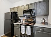 Thumbnail 2 of 45 - A black refrigerator is in a kitchen with a black stove and black microwave.