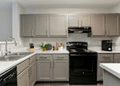 Thumbnail 7 of 13 - A kitchen with a black stove top oven and white countertops.