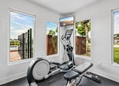 Thumbnail 14 of 33 - A home gym with a stationary bike and a view of the backyard through the windows.