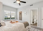 Thumbnail 10 of 70 - A bedroom with a bed, a ceiling fan, and a bathroom visible through an open door.