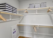 Thumbnail 9 of 29 - A white closet with clothes hanging and bins on the shelf.