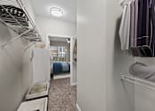 Thumbnail 12 of 52 - A white closet with clothes hanging and a bed in the background.