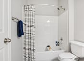 Thumbnail 16 of 70 - A white bathroom with a white toilet, white tub, and a white shower curtain.
