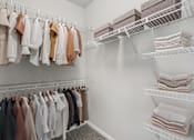 Thumbnail 27 of 70 - A white closet with clothes hanging and folded towels on shelves.