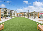 Thumbnail 18 of 29 - A grassy area in front of apartment buildings with wooden benches.