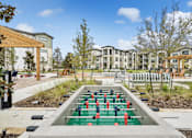 Thumbnail 17 of 29 - A foosball table sits in the middle of a courtyard with apartment buildings in the background.
