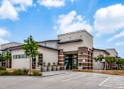 Thumbnail 34 of 36 - Modern community building exterior with brick accents, planters, and landscaped beds.