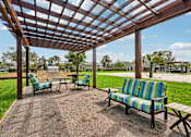Thumbnail 24 of 33 - A wooden pergola with a striped couch and two chairs.
