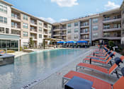 Thumbnail 22 of 49 - A pool surrounded by sun loungers and umbrellas in front of apartment buildings.
