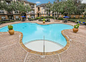 Thumbnail 25 of 27 - A large outdoor swimming pool surrounded by a concrete patio and a grassy area with trees.