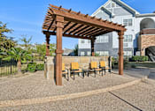 Thumbnail 56 of 70 - A wooden pergola with yellow chairs is in the foreground of a residential area.