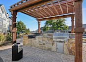 Thumbnail 57 of 70 - A wooden pergola is over a stone wall with a grill underneath it.