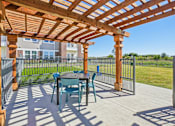 Thumbnail 32 of 43 - A wooden pergola with a table and chairs is set up on a patio.