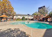 Thumbnail 26 of 35 - A large outdoor swimming pool surrounded by a patio area with chairs and a gazebo.