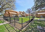 Thumbnail 31 of 45 - A black fence surrounds a green lawn in front of a brick building.