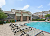 Thumbnail 23 of 32 - A pool area with sun loungers and a building in the background.