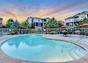 Thumbnail 17 of 22 - A swimming pool surrounded by a fence and chairs with a sunset in the background.