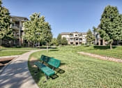 Thumbnail 21 of 22 - A park with a bench and apartment buildings in the background.