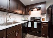 Thumbnail 5 of 28 - A kitchen with dark wood cabinets and black appliances.