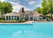 Thumbnail 1 of 13 - A large swimming pool in front of a house with a patio and chairs.