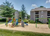 Thumbnail 13 of 13 - A playground with a slide, swings, and sandbox in front of apartment buildings.