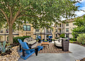 Thumbnail 23 of 35 - Outdoor lounge area with cushioned seating under a shade tree and patterned rug.