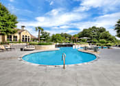 Thumbnail 15 of 35 - Resort-style pool with curved edge, stone landscaping, and wide sun deck seating.
