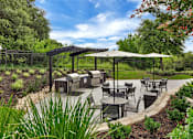 Thumbnail 25 of 35 - Landscaped patio with grills, outdoor dining tables, and shaded seating near greenery.