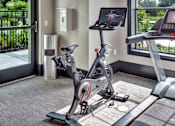 Thumbnail 32 of 35 - Indoor cardio corner with a stationary bike and treadmill beside bright windows.