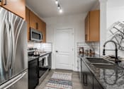 Thumbnail 7 of 35 - Galley kitchen with stainless refrigerator, range, and granite countertops with tile backsplash.