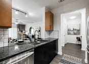 Thumbnail 6 of 35 - Modern kitchen with black cabinetry and granite counters, opening to the main living area.