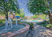 Thumbnail 21 of 25 - A fountain in the middle of a park with trees and a pool in the background.