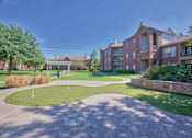 Thumbnail 22 of 25 - A large grassy area with a stone wall and apartment buildings in the background.