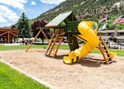 Thumbnail 3 of 18 - a yellow slide in a playground with a picnic shelter in the background