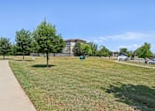 Thumbnail 29 of 36 - a park with grass and trees in front of a building