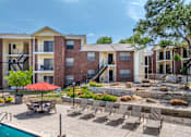 Thumbnail 21 of 30 - A pool area with chairs and a red umbrella in front of apartment buildings.