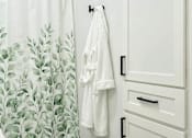 Thumbnail 30 of 31 - A white bathroom with a green rug and a shower curtain with green leaves on it.