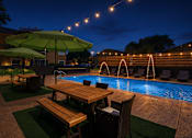 Thumbnail 31 of 31 - A poolside table with chairs and umbrellas is lit up at night.
