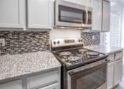 Thumbnail 9 of 15 - A modern kitchen with a stove top oven and microwave above it.