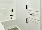 Thumbnail 29 of 31 - A white bathroom with a tub and a cabinet.