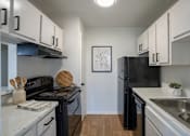 Thumbnail 14 of 27 - A black refrigerator sits in a kitchen with white cabinets.