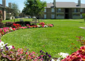 Thumbnail 1 of 3 - a lush green lawn with flowers in front of an apartment building  at Wymberly Pointe, Grand Prairie, TX, 75052
