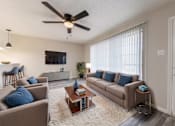 Thumbnail 2 of 5 - A living room with a brown couch, a white rug, and a ceiling fan.