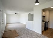 Thumbnail 15 of 27 - A room with a ceiling fan and a kitchen area in the back.