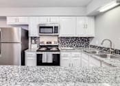 Thumbnail 6 of 15 - A kitchen with a refrigerator, microwave, oven, and sink.