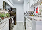 Thumbnail 2 of 12 - A kitchen with a black refrigerator and white cabinets.