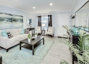 Thumbnail 6 of 12 - A living room with a white couch, a coffee table, and a painting on the wall.