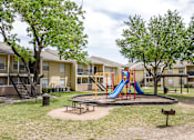 Thumbnail 11 of 12 - A playground with a slide and a picnic table in front of apartment buildings.